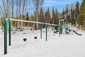 A snow-covered playground with swings and a slide. - Conveniently located condo w/ shared pool, hot tub, game room, fitness area (Winter Park)