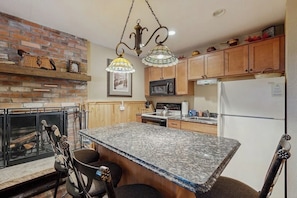 A kitchen with a granite countertop, wooden cabinets, a microwave, a refrigerator, and hanging pendant lights. - Conveniently located condo w/ shared pool, hot tub, game room, fitness area (Winter Park)