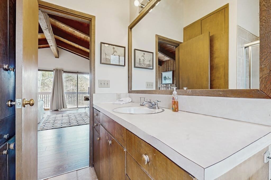 Un baño con un espejo grande, dos lavamanos, armarios de madera y vistas a un balcón.