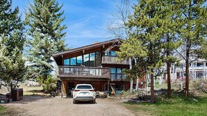 A two-story building with a balcony, a car parked in front, and trees around. - Spacious Mountain Lodge-Style Home with Free WiFi - Nearby Ski Access (Aspen)