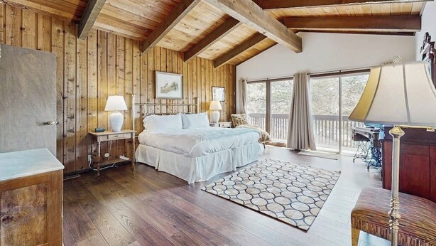 A wooden-paneled bedroom with a bed, two bedside lamps, a rug, and a window with curtains. - Spacious Mountain Lodge-Style Home with Free WiFi - Nearby Ski Access (Aspen)