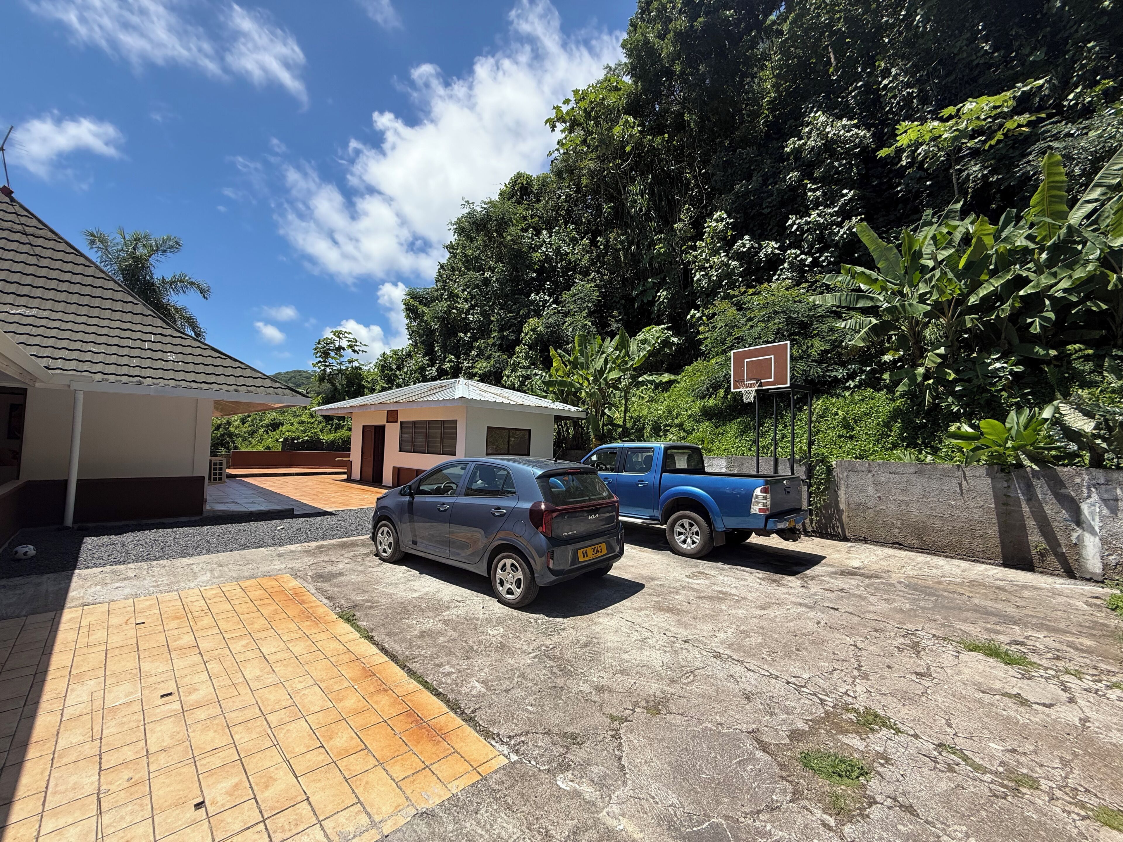 A residential area with a house, a basketball court, and two parked cars.