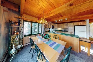 Ein Holzblock-Innenraum mit Esstisch, Stühlen, einer Chandelüster und einer Küchenzeile.