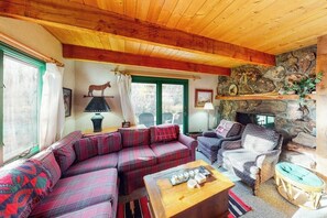 Ein gemütliches Wohnzimmer mit Holzbalkendecke, einem Steinkamin, einem Sofa, einem Sessel und einem Tisch mit Dekoration.