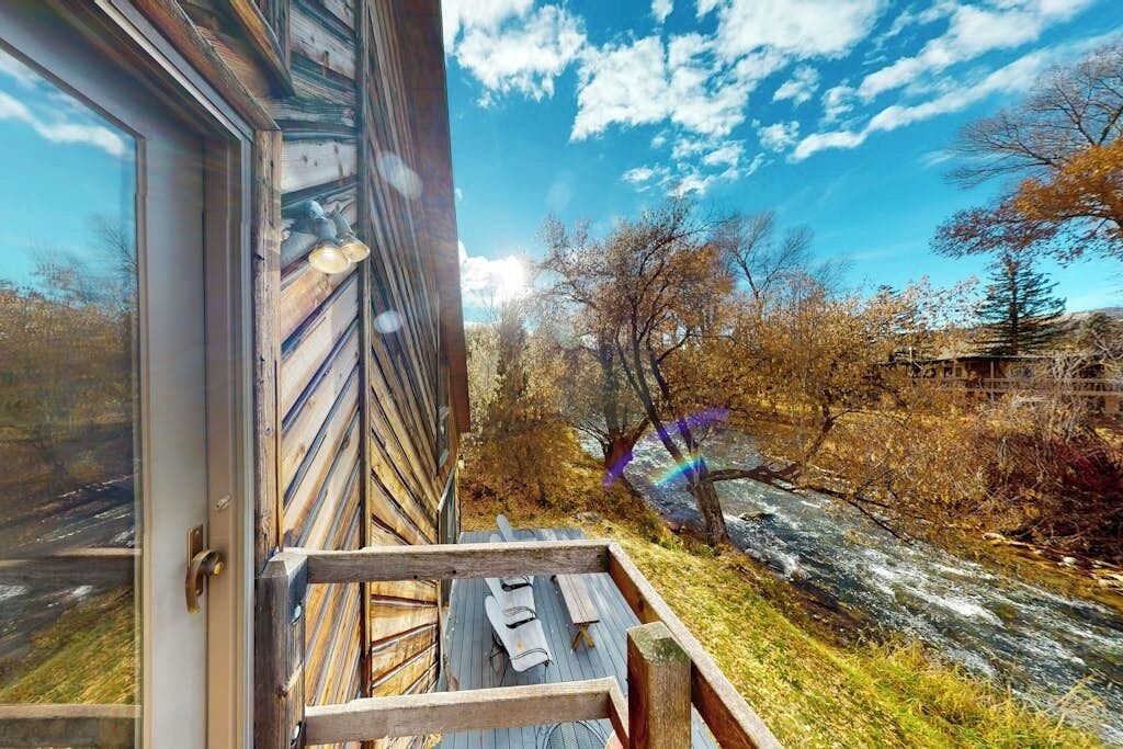 A wooden deck with a bench and a table, overlooking a river and trees.