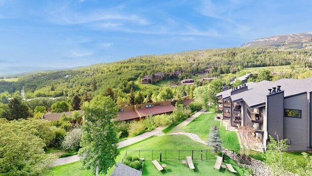 Quartiere residenziale con case moderne, un prato curato e vista libera sui colli boscosi circostanti.