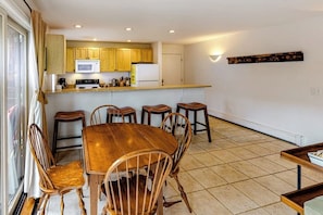 A dining area with a wooden table and chairs, a kitchen with wooden cabinets, a microwave, and a refrigerator.