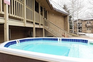 A swimming pool with a blue tiled edge, a wooden deck, and a staircase leading to a balcony.