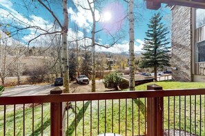 Blick von einem Balkon auf eine Auffahrt mit parkenden Autos, ein Steinhaus und einen klaren Himmel.