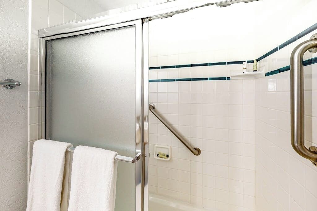 Un baño con puerta de vidrio, azulejos blancos, un pasamanos y un perchero para toallas.