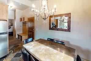 A dining area with a large table, chairs, a chandelier, and a mirror on the wall.