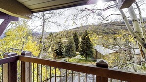 Ein Holzbalkon mit Blick auf eine gebirgige Landschaft, Bäume und ein Gebäude in der Ferne.
