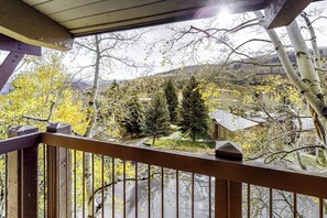 Ein Holzbalkon mit Blick auf eine gebirgige Landschaft, Bäume und ein Gebäude in der Ferne.