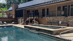 Ein Swimmingpool mit Liegestühlen, einer Treppe und einem Gebäude mit steinverkleideter Fassade.