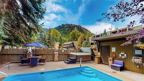 Un área de piscina con jacuzzi, asientos exteriores y montañas al fondo.