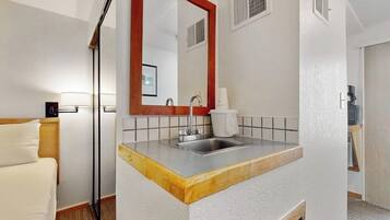 A hotel room with a wooden bed, a white sink with a red-framed mirror, and a white tiled backsplash.