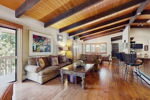 A spacious living area with a wooden ceiling, a sofa set, a coffee table, and a bar area with stools.