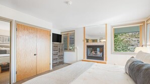 Een slaapkamer met een bed, een open haard, een kledingkast en een raam met jaloezieën.