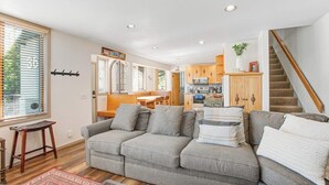 Een moderne woonkamer met een grijze bank, houten vloeren en een trap.