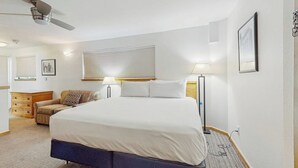 Una camera d'albergo con un letto, comodini, una ventola a soffitto, una finestra con tende e una TV fissata al muro.