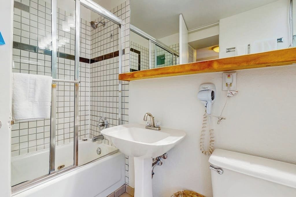 A bathroom with a bathtub, a sink, a hairdryer, and a toilet.