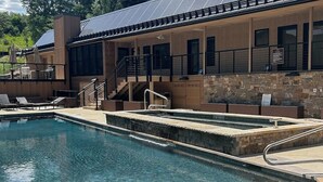 Ein Swimmingpool mit Liegestühlen, einer Treppe und einem Gebäude mit steinverkleideter Fassade.