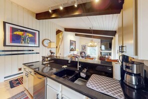 A modern kitchen with a black countertop, stainless steel appliances, and a wooden ceiling. - Lovely home near skiing with fireplace, balcony, & chic decor (Snowmass Village)