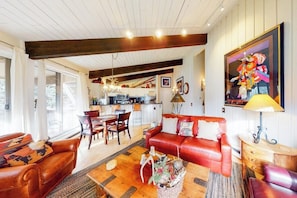 A spacious living room with a red sofa, wooden coffee table, and a dining area with chairs and a table. - Lovely home near skiing with fireplace, balcony, & chic decor (Snowmass Village)
