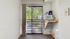 Una habitación con puerta corredera que da a un balcón, un microondas en un estante y un termostato en la pared.