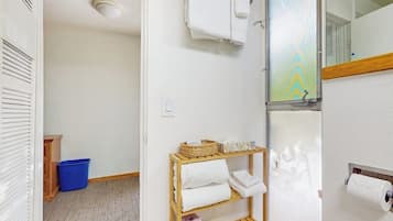 Een badkamer met een douche, een handdoekhouder, een toiletpapierhouder en een blauwe prullenbak.