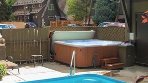Een achtertuin met een zwembad, hottub en een houten terras.