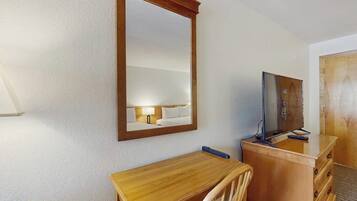 A hotel room with a wooden desk, a chair, a television on a wooden cabinet, and a large mirror on the wall.