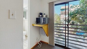 Een kleine kamer met een schuifglasdeur naar een balkon, een magnetron op een plank, en een stopcontact.