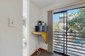 Una habitación pequeña con una puerta de vidrio corredera a un balcón, un microondas en un estante y un enchufe.