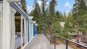 A wooden deck with a railing, overlooking a forested area. - Dog-OK, updated home with WiFi, Sauna,  game room - close to lakes & hiking (Lake Arrowhead)