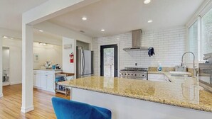 A modern kitchen with white cabinetry, a granite countertop, and a central island with bar seating. - Dog-OK, updated home with WiFi, Sauna,  game room - close to lakes & hiking (Lake Arrowhead)