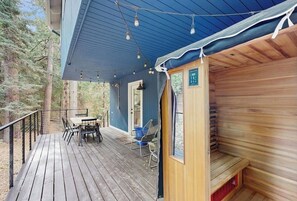 Een houten terras met een tafel, stoelen, een sauna en uitzicht op het omliggende bos.