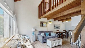 Amplia sala de estar con techo de madera, un conjunto de sofás, una mesa de comedor con sillas y una escalera.