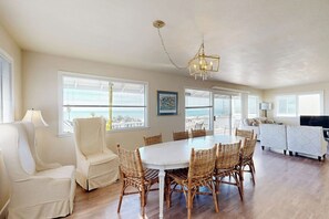 A spacious room with a large dining table surrounded by wicker chairs, a white sofa, and a television. - Charming, two-story home with deck, grill, and ocean views (Cayucos)