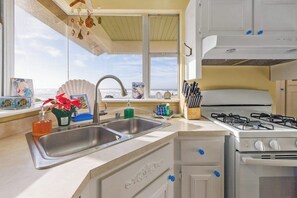 A kitchen with a double sink, a gas stove, and a window with a view of the sea.