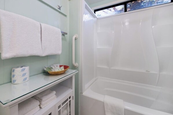 A bathroom with a glass shower enclosure, a glass shelf with toiletries, and a white towel rack. - Lovely Beachfront Home with Stunning Ocean Views & Private Yard (Cayucos)