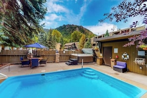 A pool area with a hot tub, outdoor seating, and a mountain backdrop.
