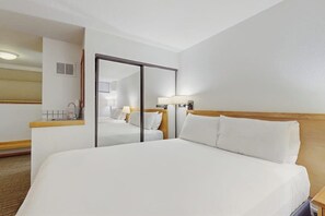 A hotel room with a large bed, a bedside table, a mirror, and a lamp.