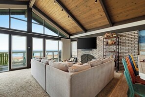 Ein großzügiges Wohnzimmer mit Ecksofa, Kamin, Fernseher und Meerblick.