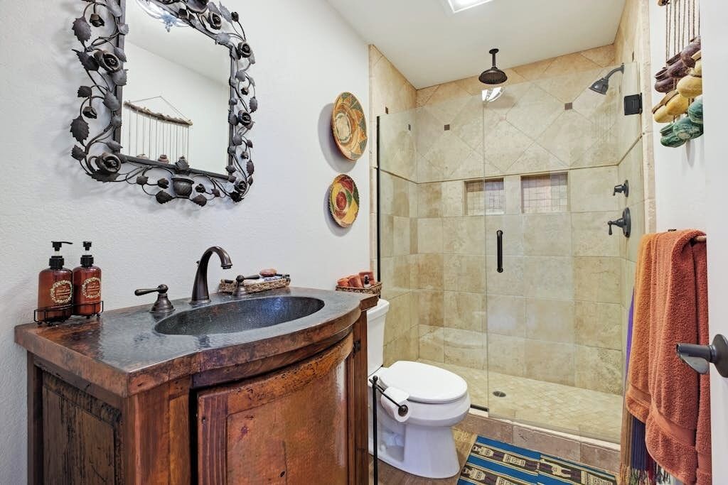 A bathroom with a wooden vanity, a sink, a mirror, a toilet, and a shower area.
