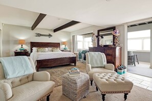 Ein Schlafzimmer mit einem Bett, zwei Stühlen, einem Pouf, einem Schminktisch und einem Spiegel.