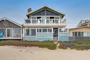 Ein zweigeschossiges Strandhaus mit Balkon, großen Fenstern und einer Holzterrasse.
