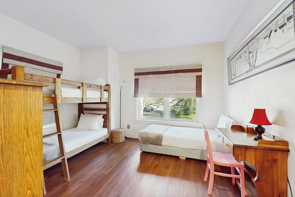 A dormitory room with bunk beds, a desk, a chair, and a window with a view.
