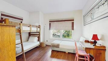 A dormitory room with bunk beds, a desk, a chair, and a window with a view.