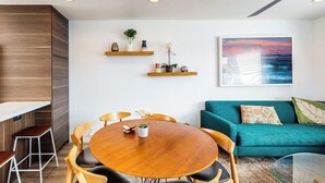 Een moderne woonkamer met een ronde houten tafel, een blauwgroene bank en een plafondventilator.